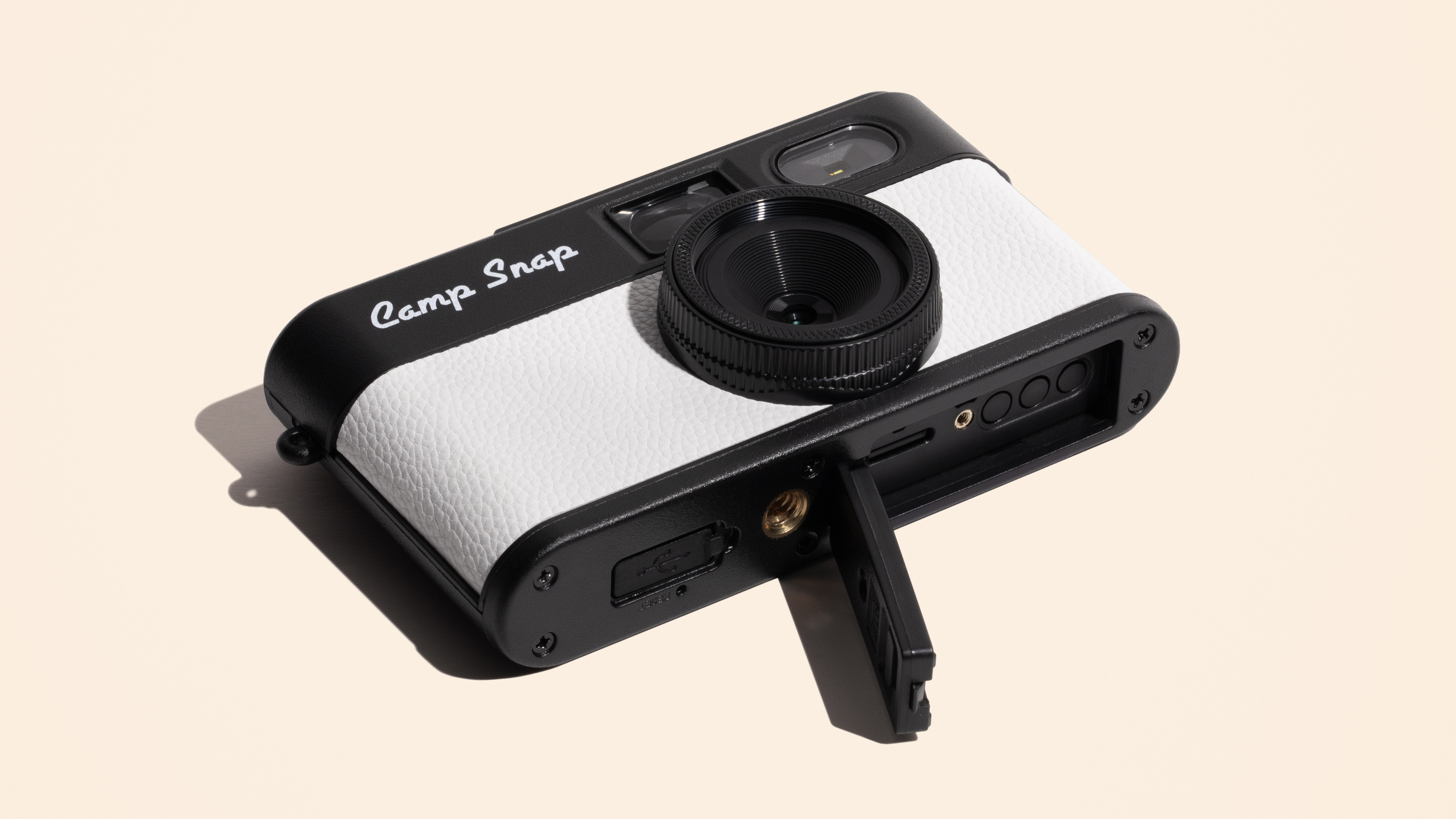 Photograph of Camp Snap 2 small digital compact camera in white, with bottom plate showing open memory card door and tripod screw mount