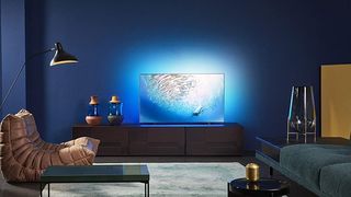 En Philips OLED 806 står på en TV-bänk med blå belysning bakom sig.