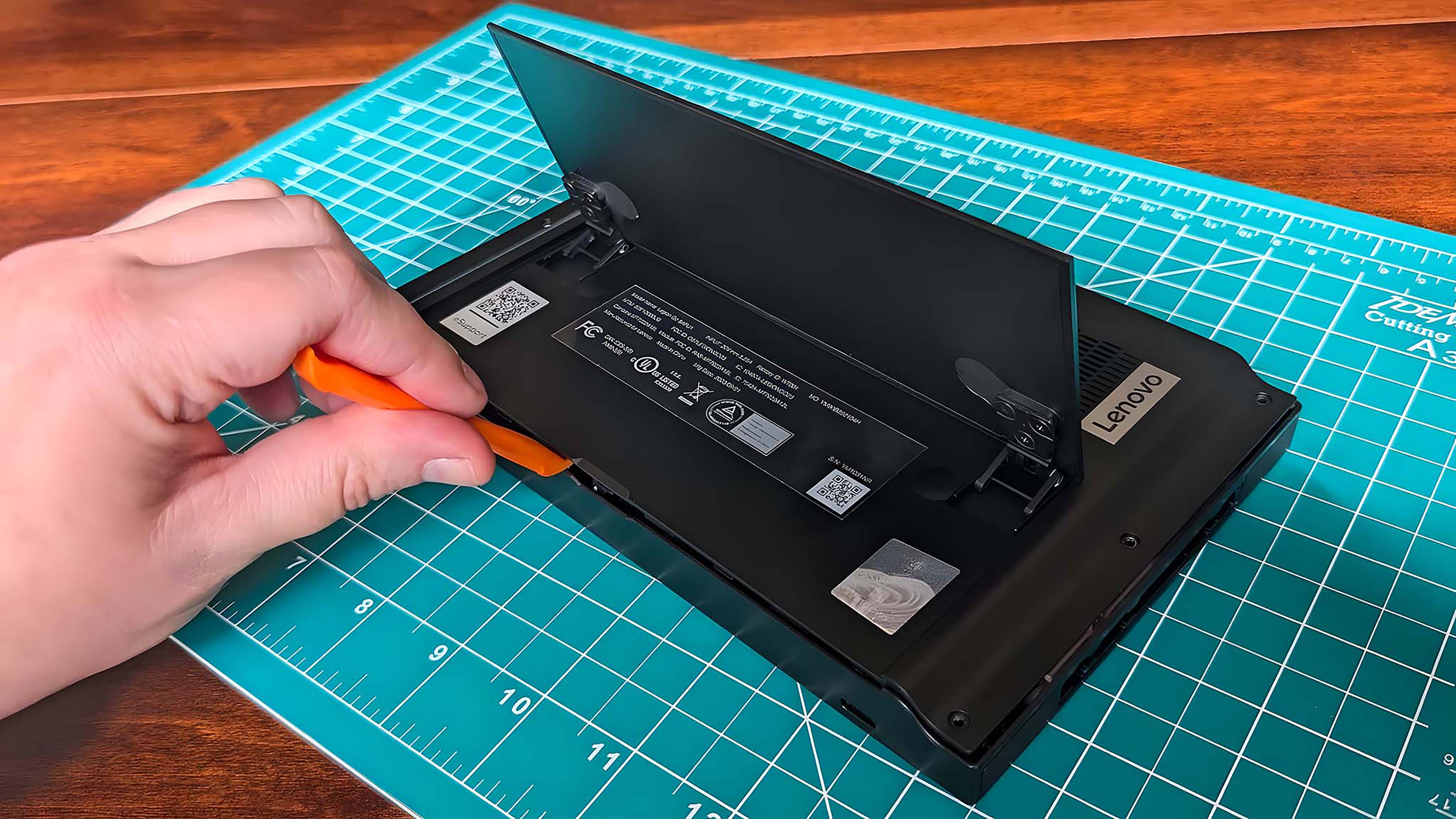 A hand using a prying tool to lift up the casing under the Lenovo Legion Go's kickstand.