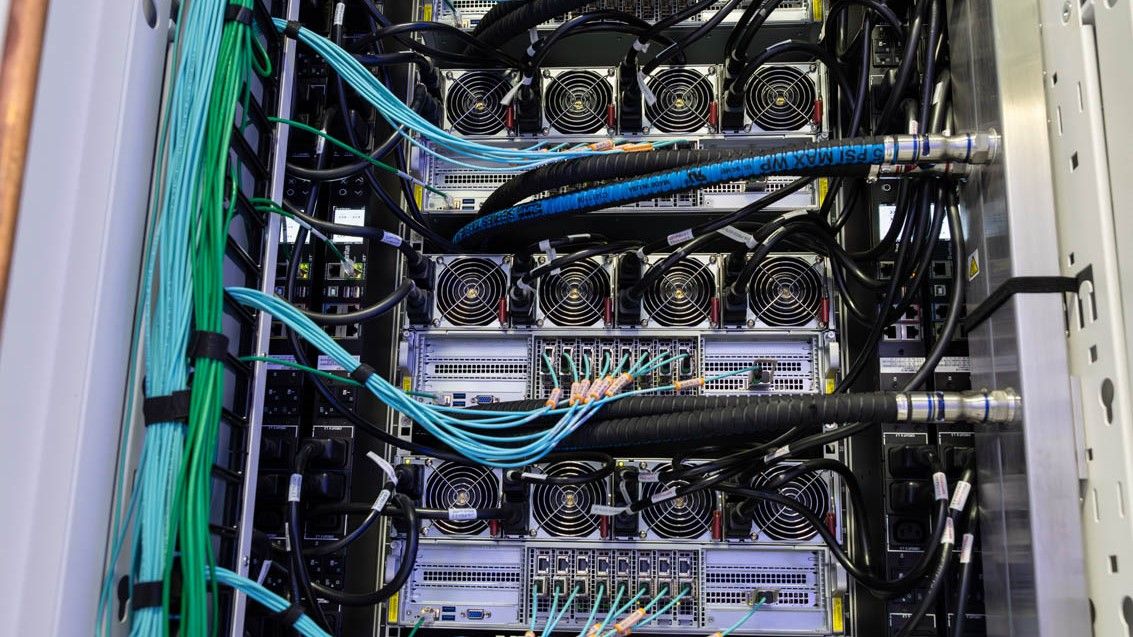 The rear access of an xAI Colossus GPU server. Nine ethernet cables emerge from each server, with four power supplies in each. Power and liquid cooling hoses are also visible.