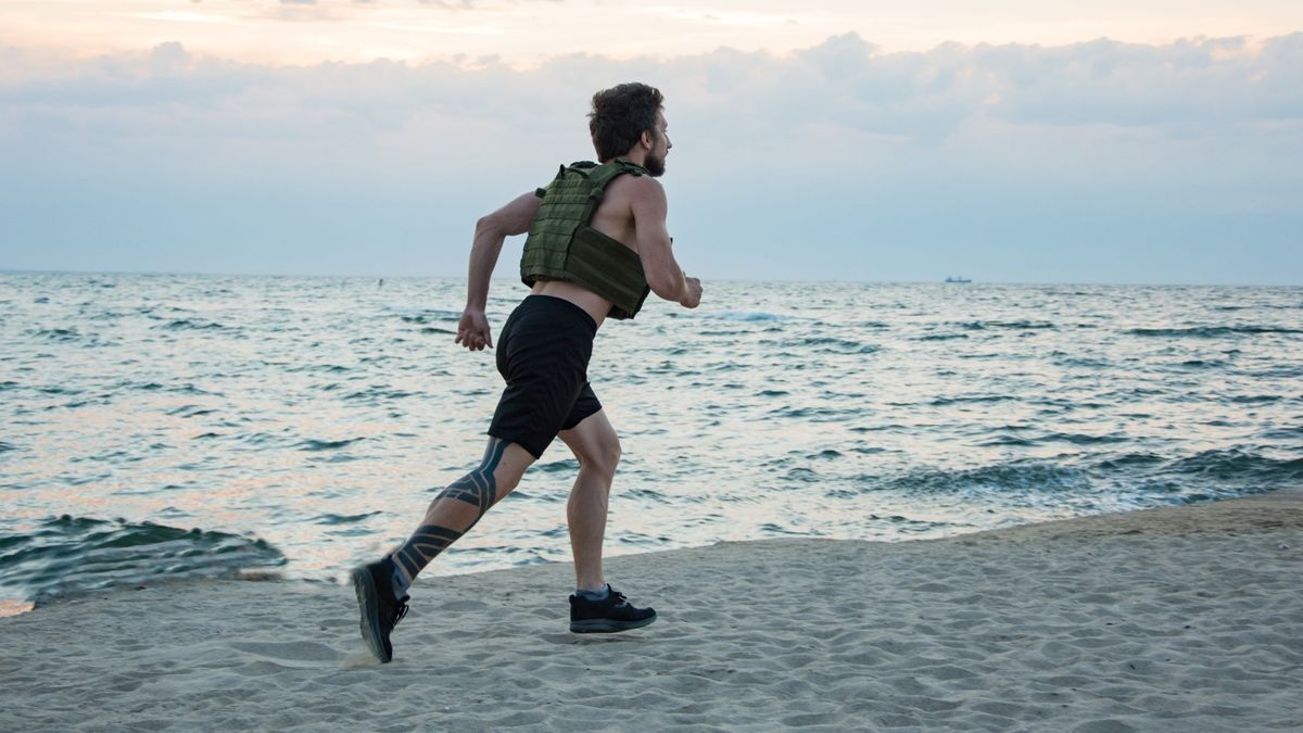 Male running along a beach wearing a weighted vest