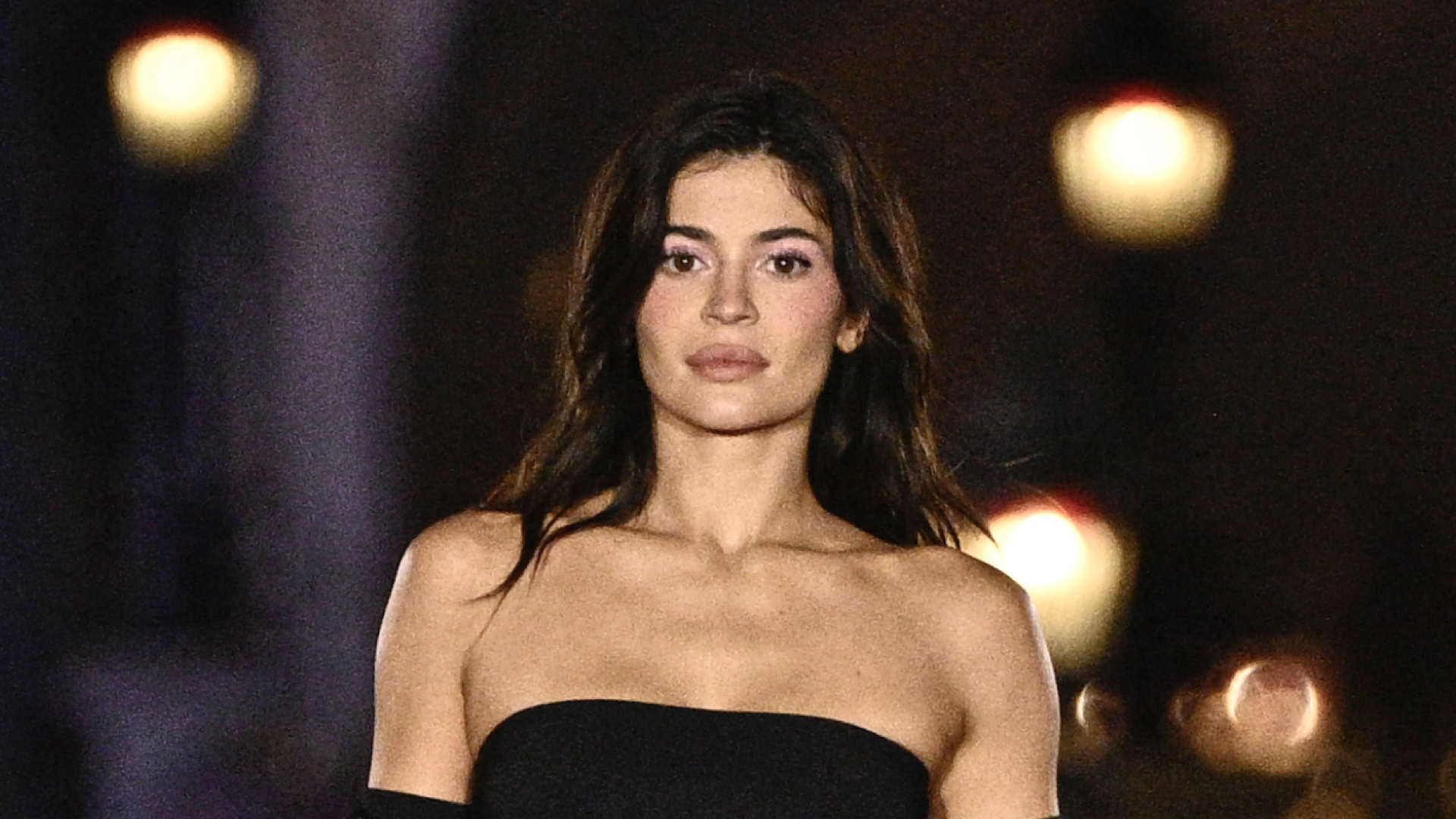 Kylie Jenner wears a strapless black gown and long black gloves as she walks the runway in front of the Disney castle