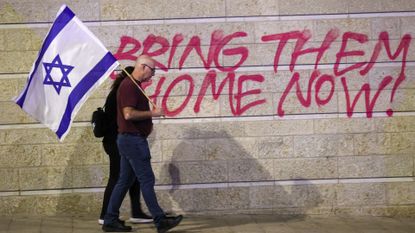 A couple holding an Israel flag walk past a protest wall