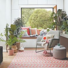 A living room with a large window, a window seat and houseplant, all tied together with a patterned rug