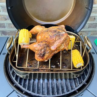 a close up of a barbecue grill with a roast chicken and corn on the cob