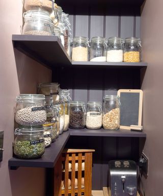 A corner pantry with corner shelves, painted in dark colors