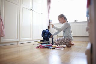 Girl kneeling on floor packing school bag