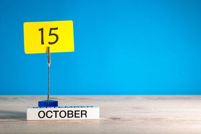 desk photo holder holding up the number 15 on a bright yellow notecard, with an October block underneath against a bright blue background