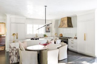 A light white kitchen with an island and dining table, wooden floor and brass hardware