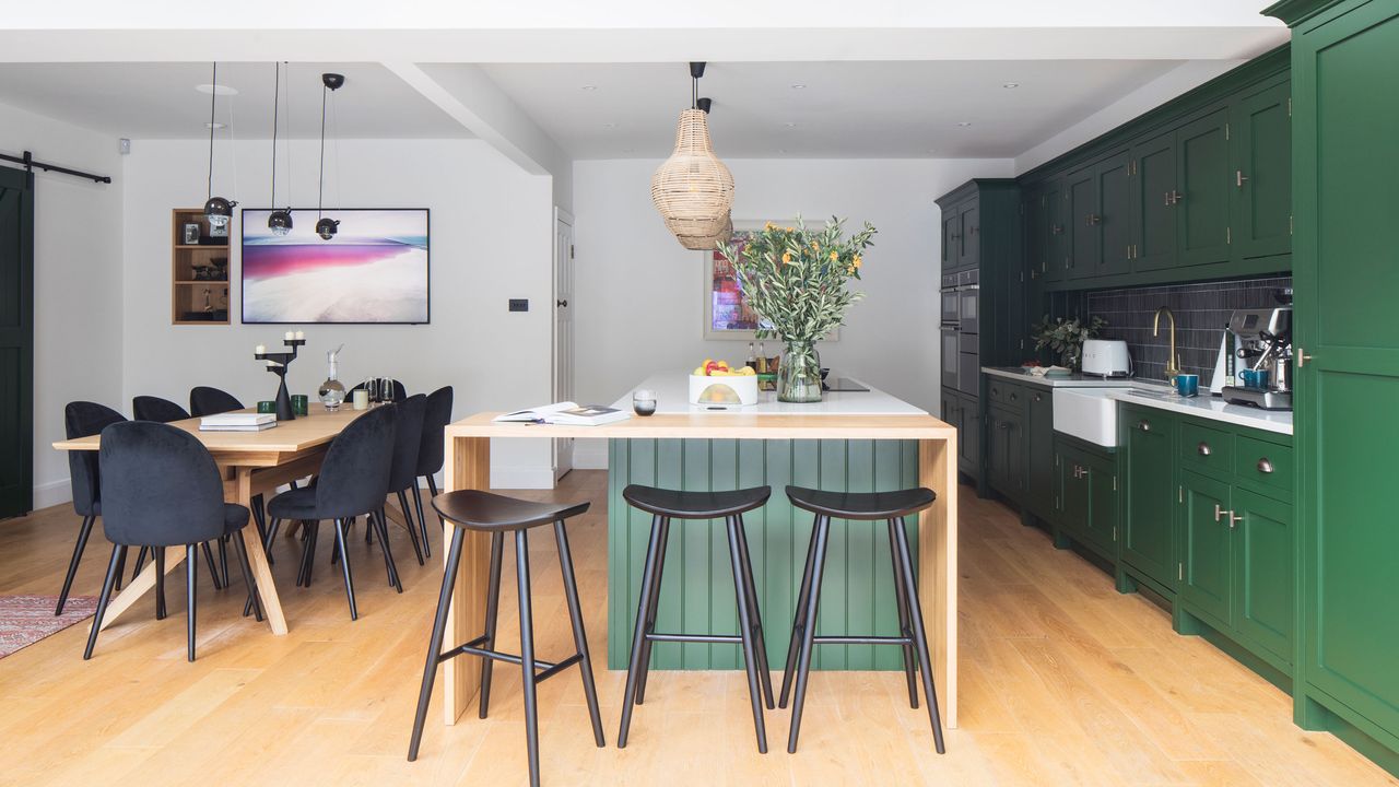 Kitchen-diner with green units and a green island with wooden breakfast bar and black stools