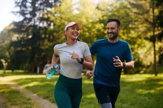 A happy couple running together outside in a park.