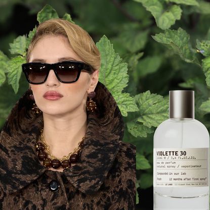 A blonde woman wearing oversized sunglasses, a brown coat, and brown jewelry. She is in front of a background of patchouli leaves and is next to three perfume bottles from Le Labo, Dolce and Gabbana, and Krigler