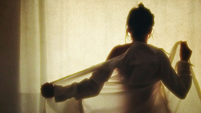 Silhouette of woman from behind taking off a shirt.