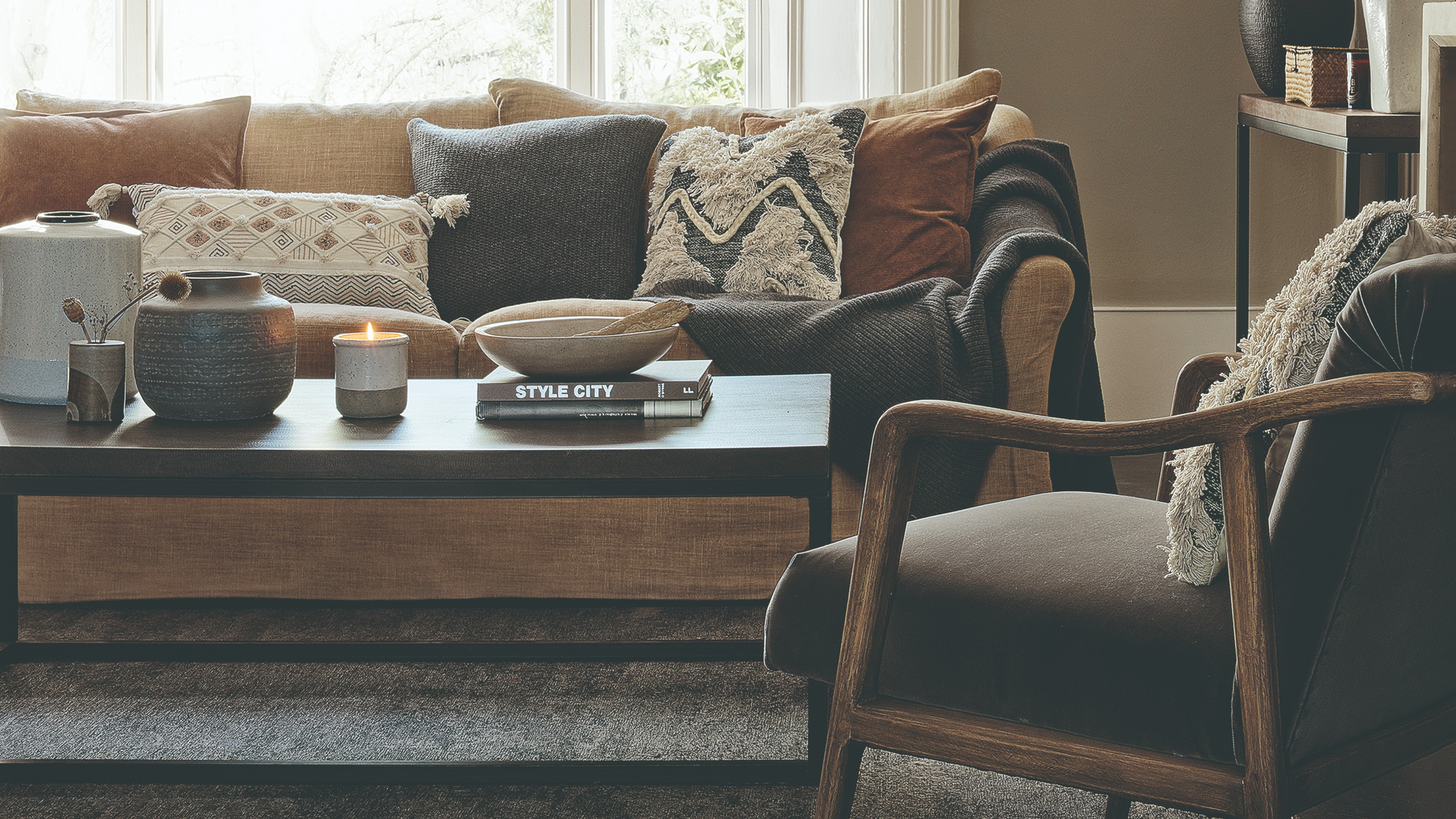 A living room with a brown sofa and textured cushions and a lit scented candle on the black coffee table