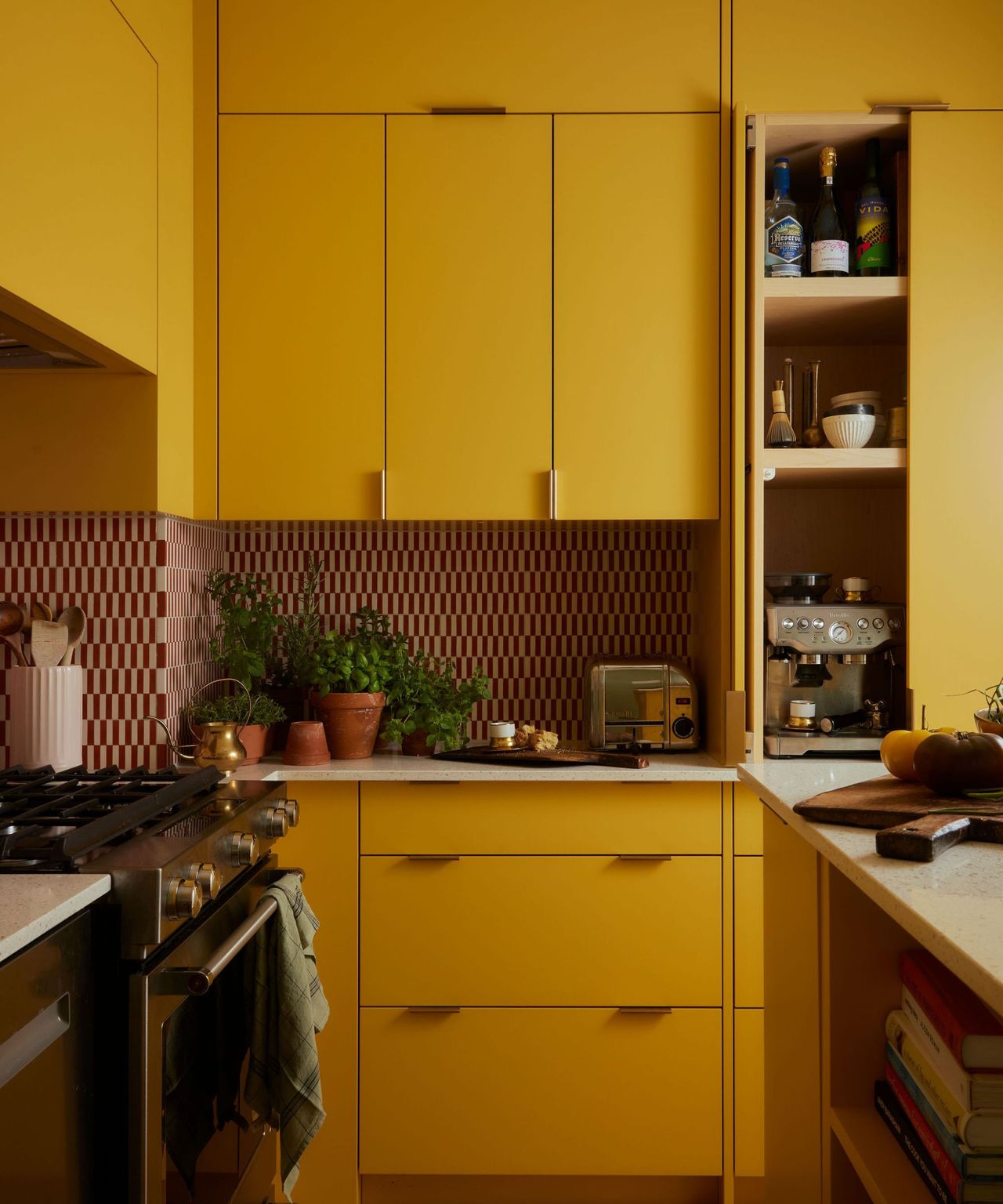 Close-up of a sunny yellow kitchen counter with a stove, a toaster, potted herbs, and an open cabinet revealing dishes and bottles