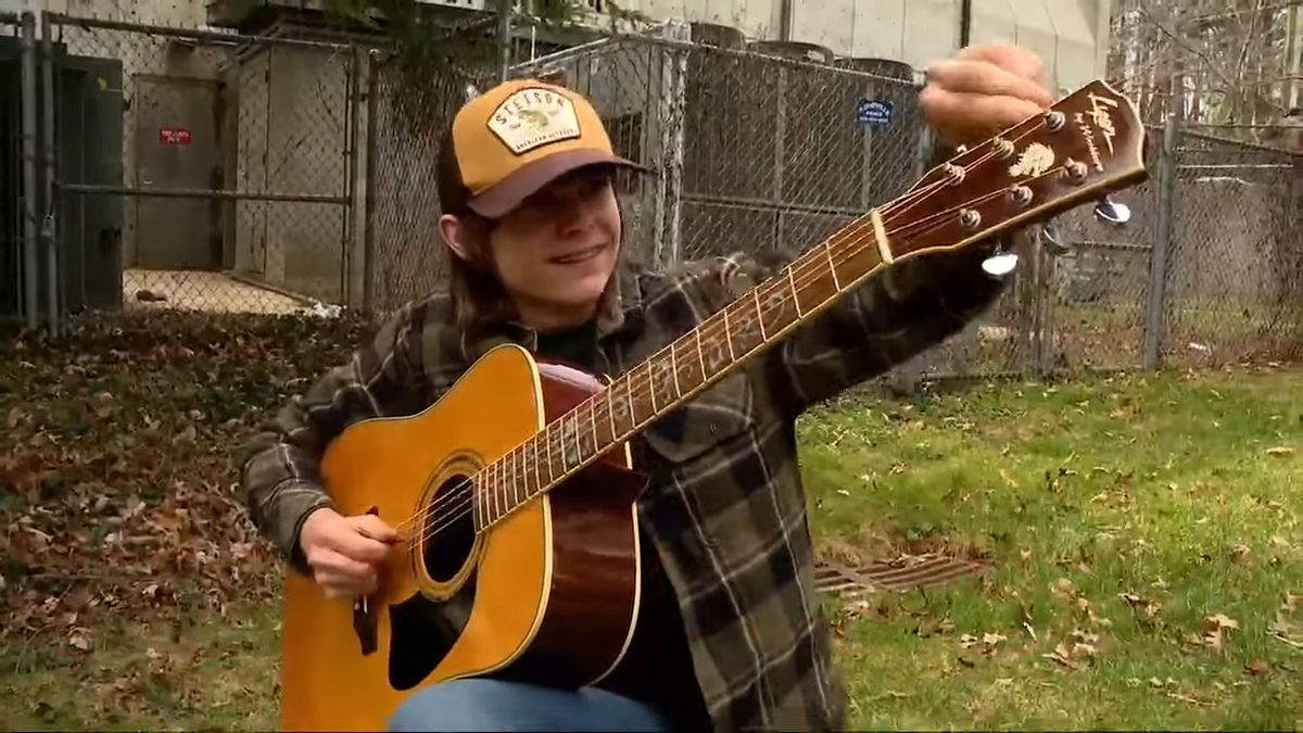 A happy young boy tunes an acoustic guitar