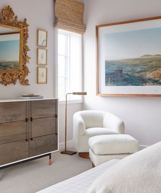 corner of relaxing bedroom with pale lilac walls, white armchair with footstool, large landscape picture on wall