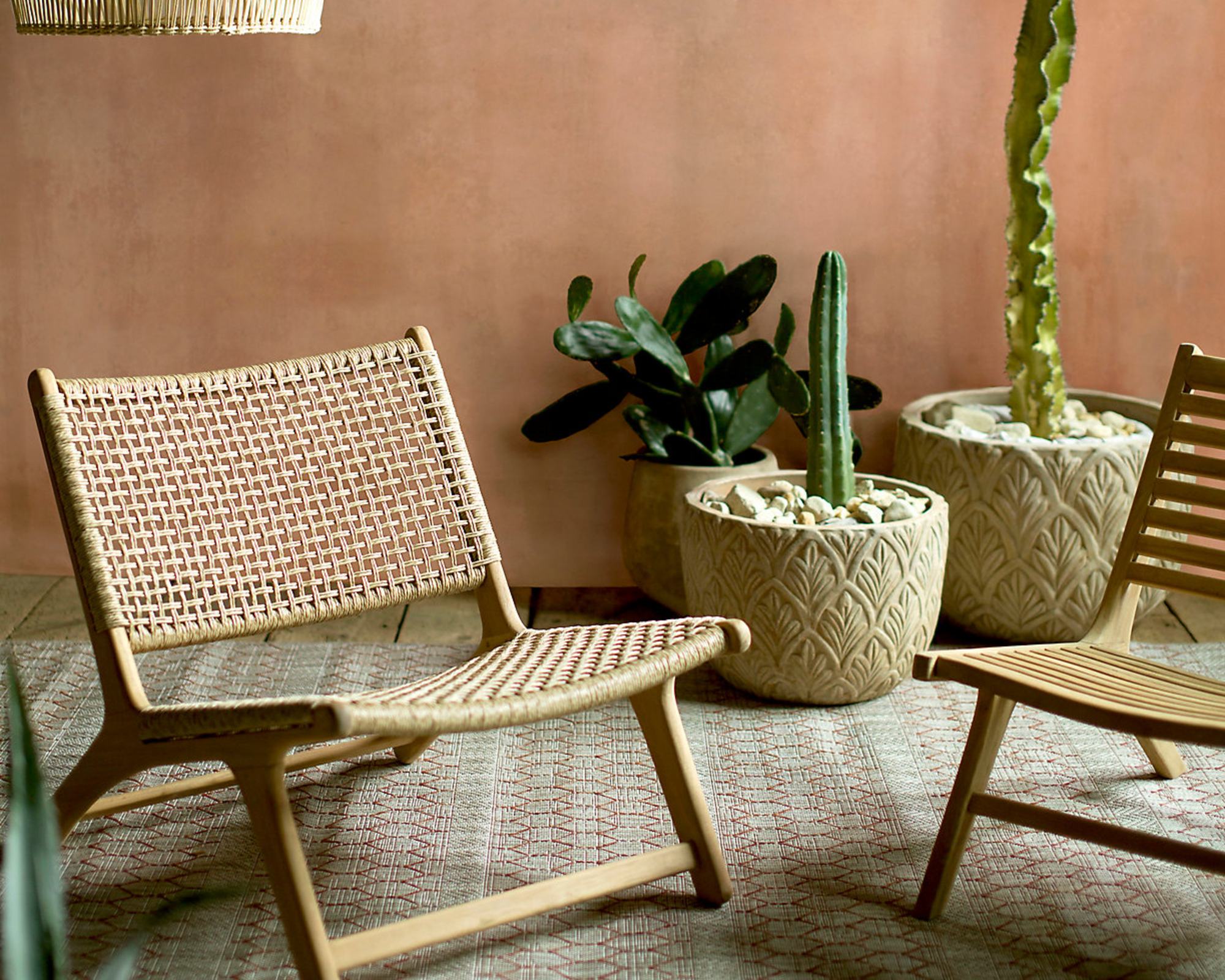 A woven outdoor lounge chair in a backyard with a terracotta-colored wall and cacti