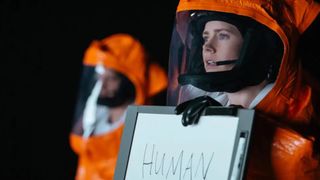 Amy Adams as Louise Banks wearing an orange suit and holding up a sign that says "Human", during the sci-fi movie, Arrival.