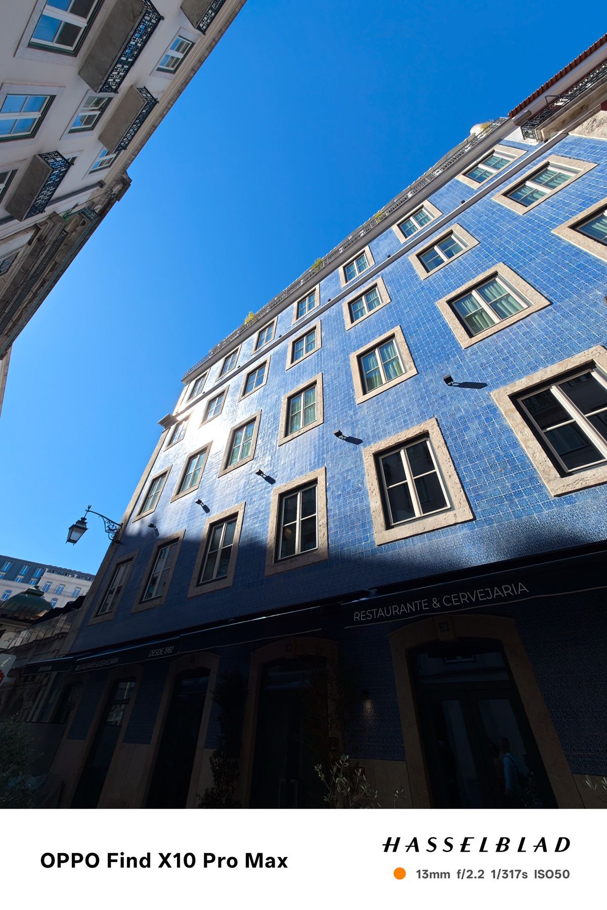 Low-angle view of a tall blue tiled building rising into a clear blue sky in Lisbon.