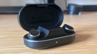 Cambridge Audio M100 earbuds in charging case on a wooden desk