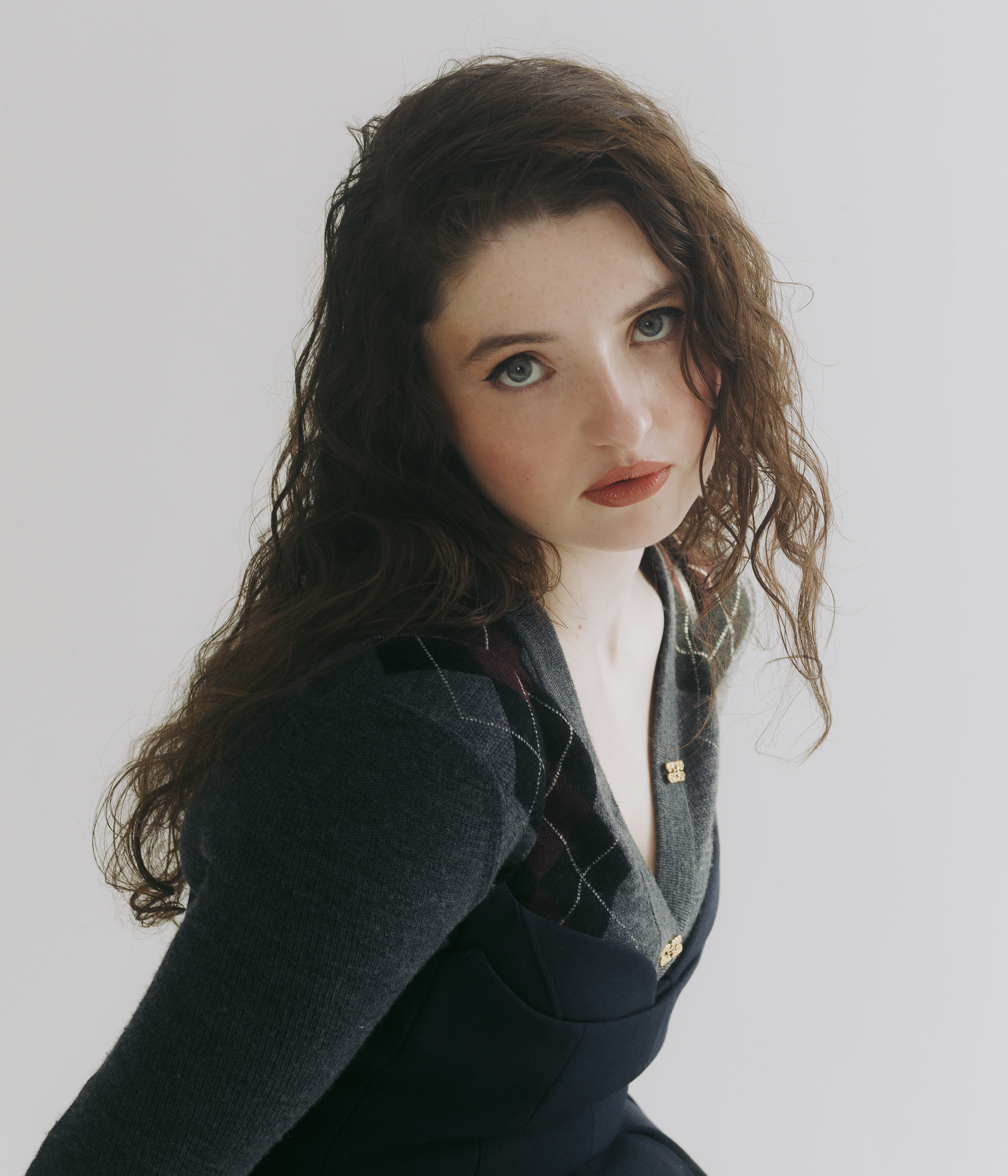 the testaments actress lucy halliday poses in a headshot wearing an argyle sweater and leaning forward