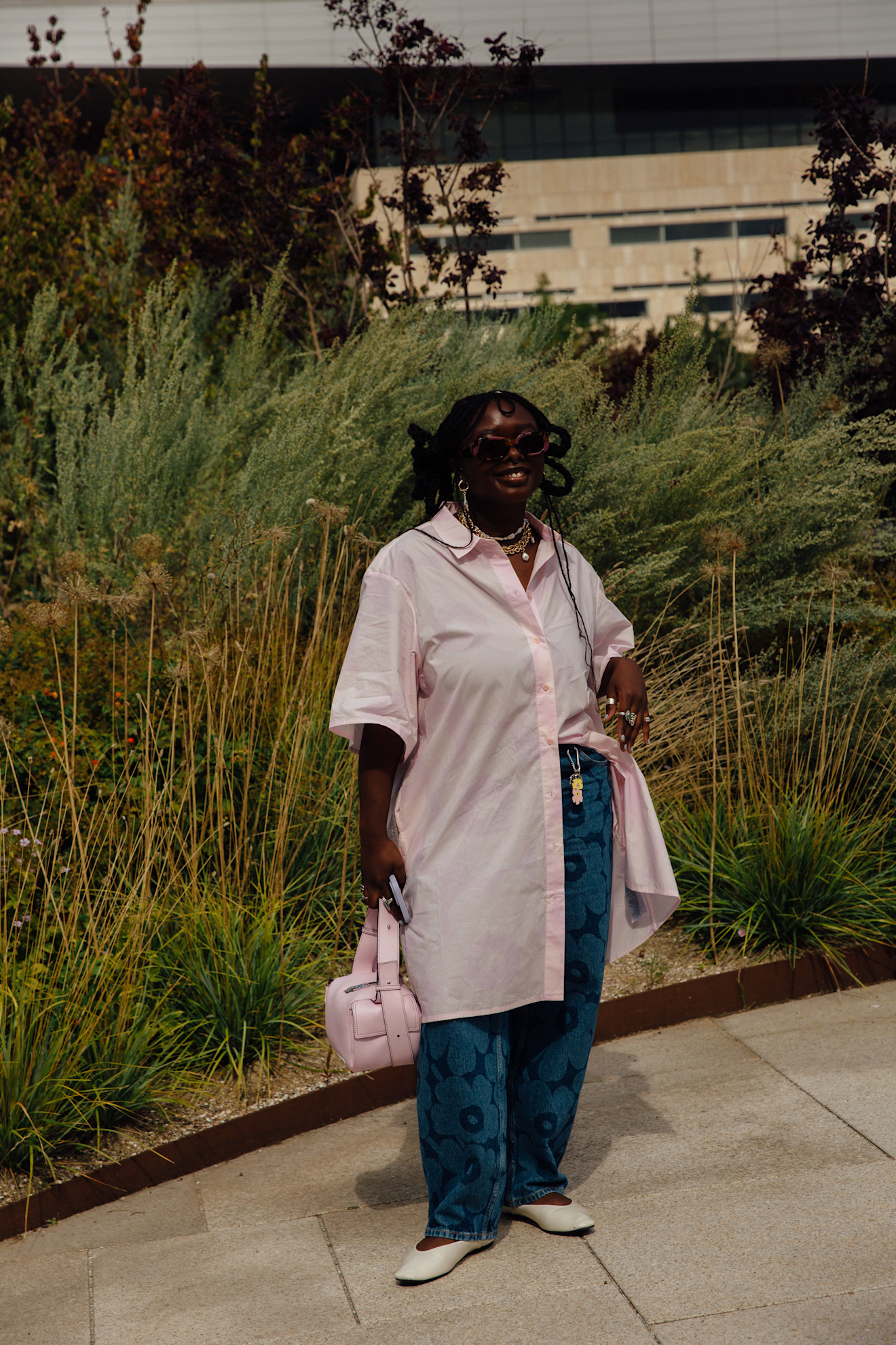 fashion week attendee wears long pink top, jeans, and white ballet flats