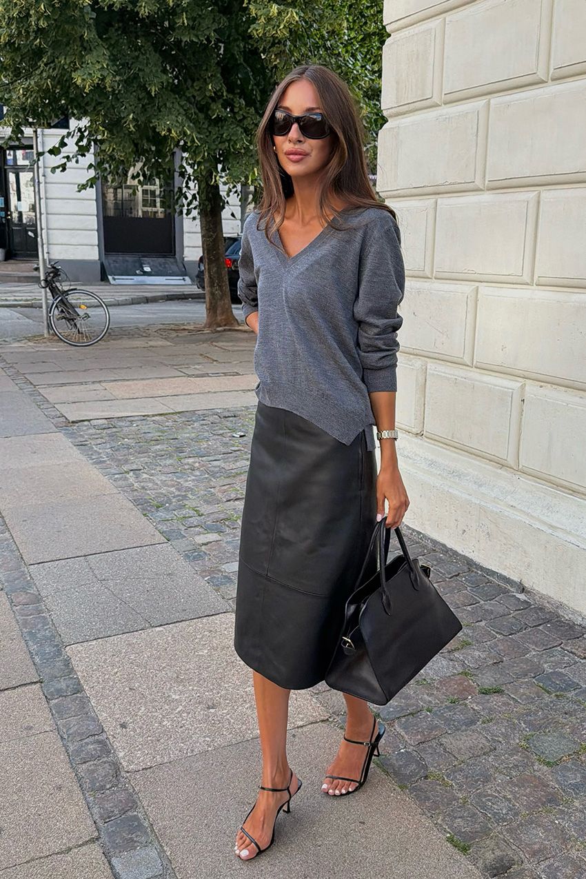 A woman wearing a gray V-neck sweater styled with a black leather pencil skirt, black sandals, and a black bowler bag.