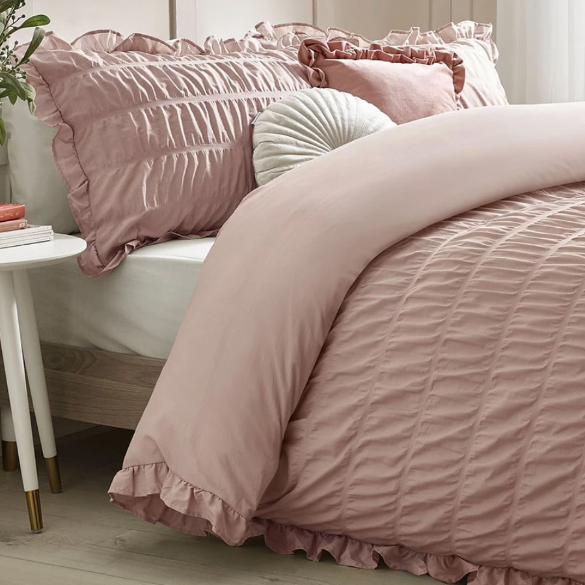 Pink ruffled bedding paired with white fitted sheet and styled on a double bed in a white room
