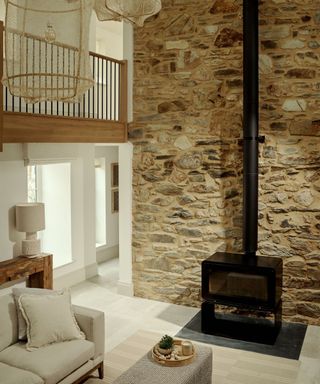 coastal style cottage home with a wall of exposed stone with a large log burner and 2 woven seagrass ceiling lights