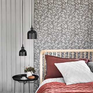 A bedroom with grey panelled walls, a wooden bedframe with burgundy and white bedding on top, and a grey and white botanical print wallpaper behind the bed