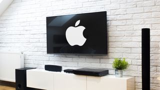 A TV mounted on a white brick wall above a contemporary media console. The screen of the TV is displaying the Apple logo in white.