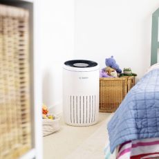 A white Bosch air purifier in a children's bedroom by the side of bed with striped bedding