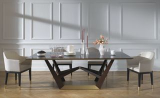 A side-on shot of a large dining table with white crockery and four low-back dining chairs.