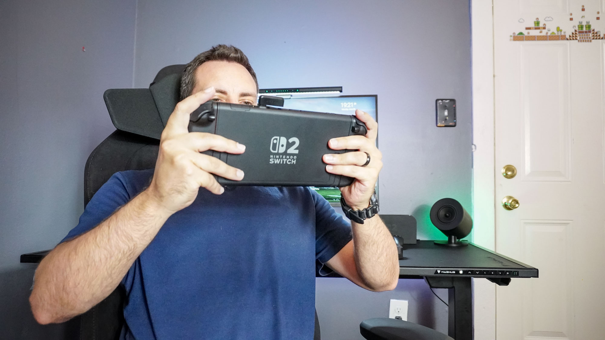 A person sitting in a gaming chair with the Razer Clio wireless speaker head cushion attached to its headrest playing Nintendo Switch 2 in handheld mode