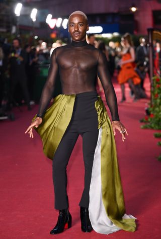 Ncuti Gatwa attends the Vogue World event in London wearing a mesh top and black dress trousers with a green satin train