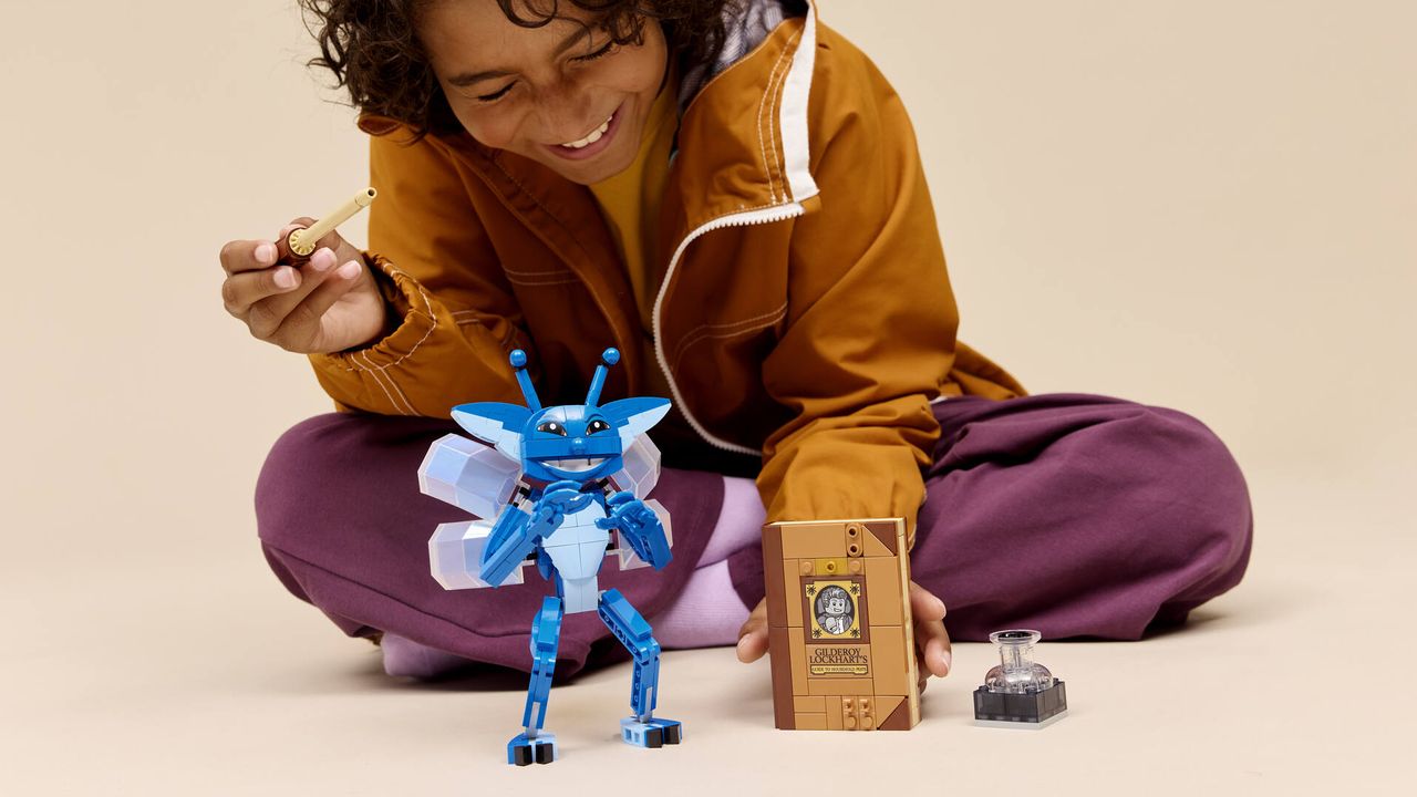A child smiles while playing with a blue pixie and Lego book