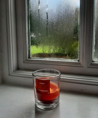 a cinnamon candle on a windowsill where the windows have condensation on the panes