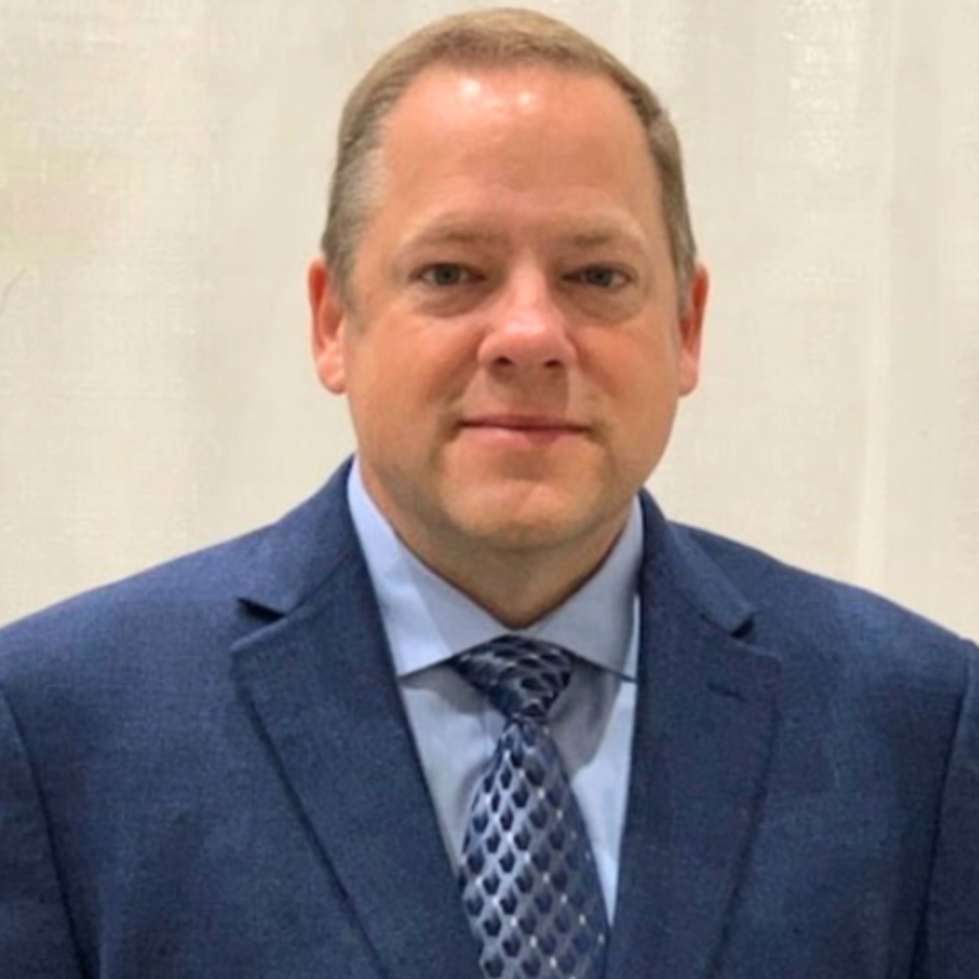 Brian Dunagan is a white man with short dark blonde hair, and is pictured wearing a blue suit, tie and shirt