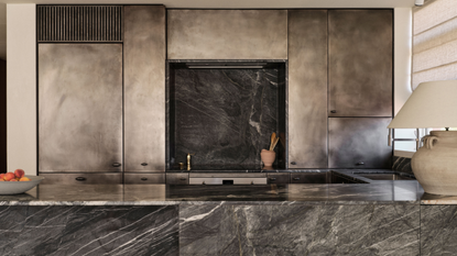 blackened steel cabinetry in a kitchen with dark, moody marble on the island and backsplash