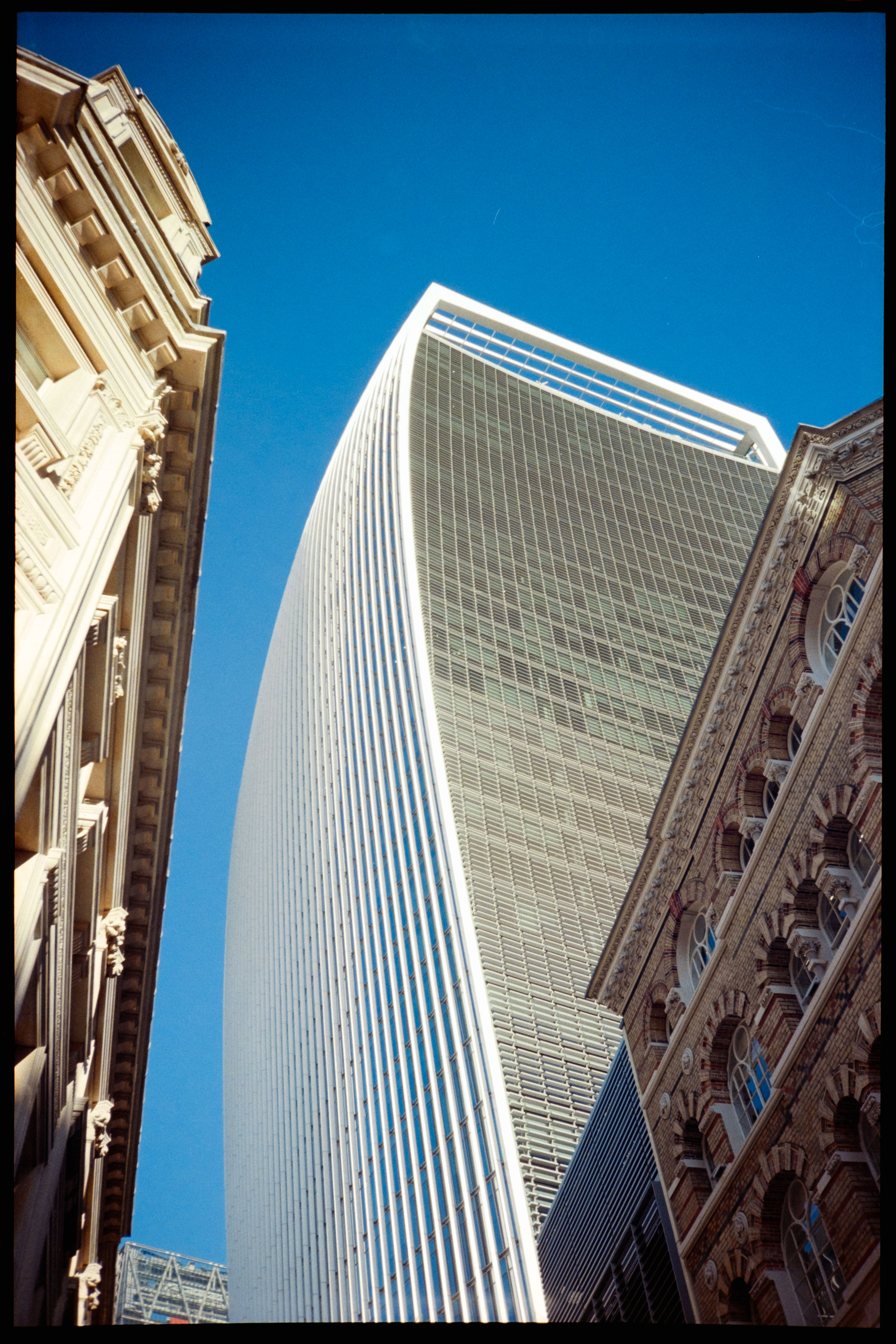 A tall skyscraper in London between two other buildings in front of a blue sky