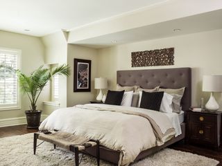 cream bedroom with brown bed, mahogany side tables, plant, artwork, blinds, cream bedding