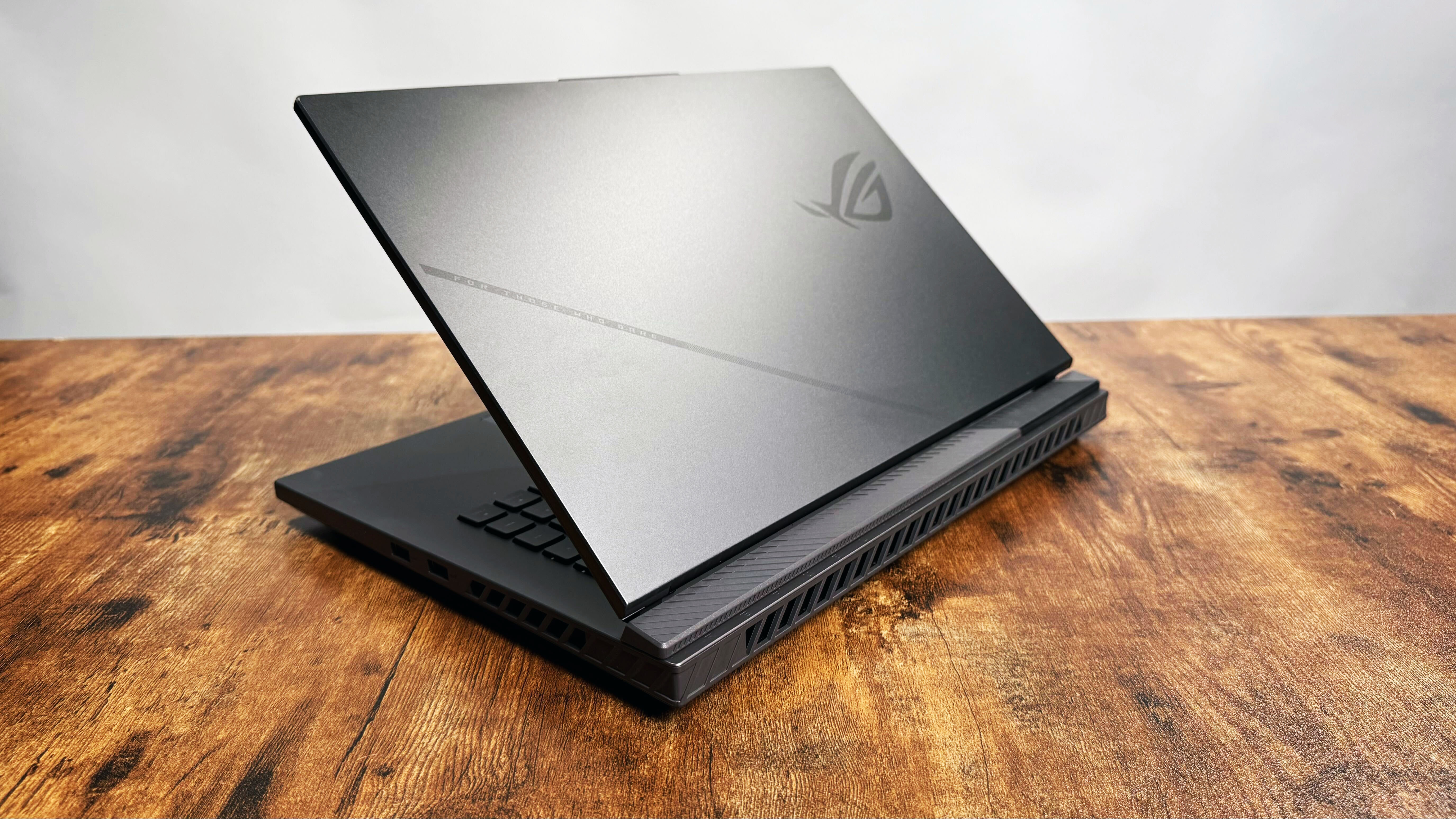 Asus ROG Strix G16 (G614FR) gaming laptop on a wooden desk against a gray background.