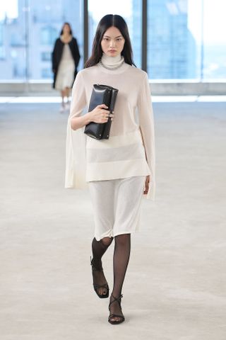 A model walks the Toteme spring/summer 2025 runway wearing a high neckline top.