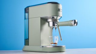 DeLonghi Dedica Duo in the green colorway with accessories photographed on a blue background. 