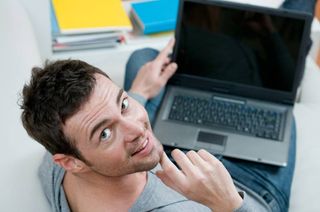 Smiling young man looking back at camera while working on laptop at home 