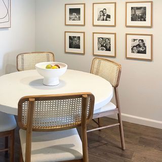 A dining table and wicker chairs in an apartment with white walls and simple black and white gallery wall