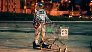 Astronaut pushes empty shopping trolley in retail car park: retail future concept