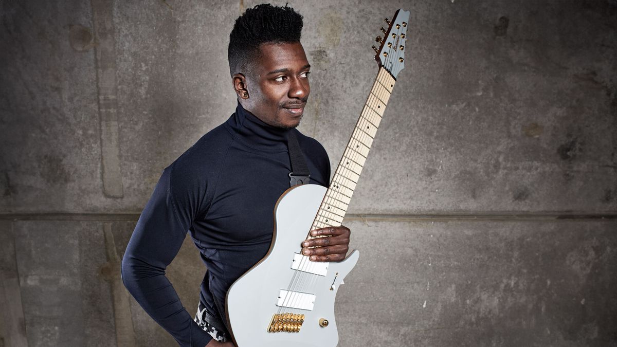 Tosin Abasi holds his Ibanez signature guitar against a grey background