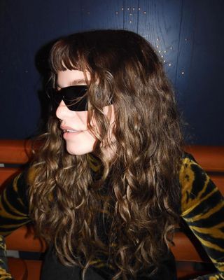 A woman with curly dark hair and sunglasses looking to the side.